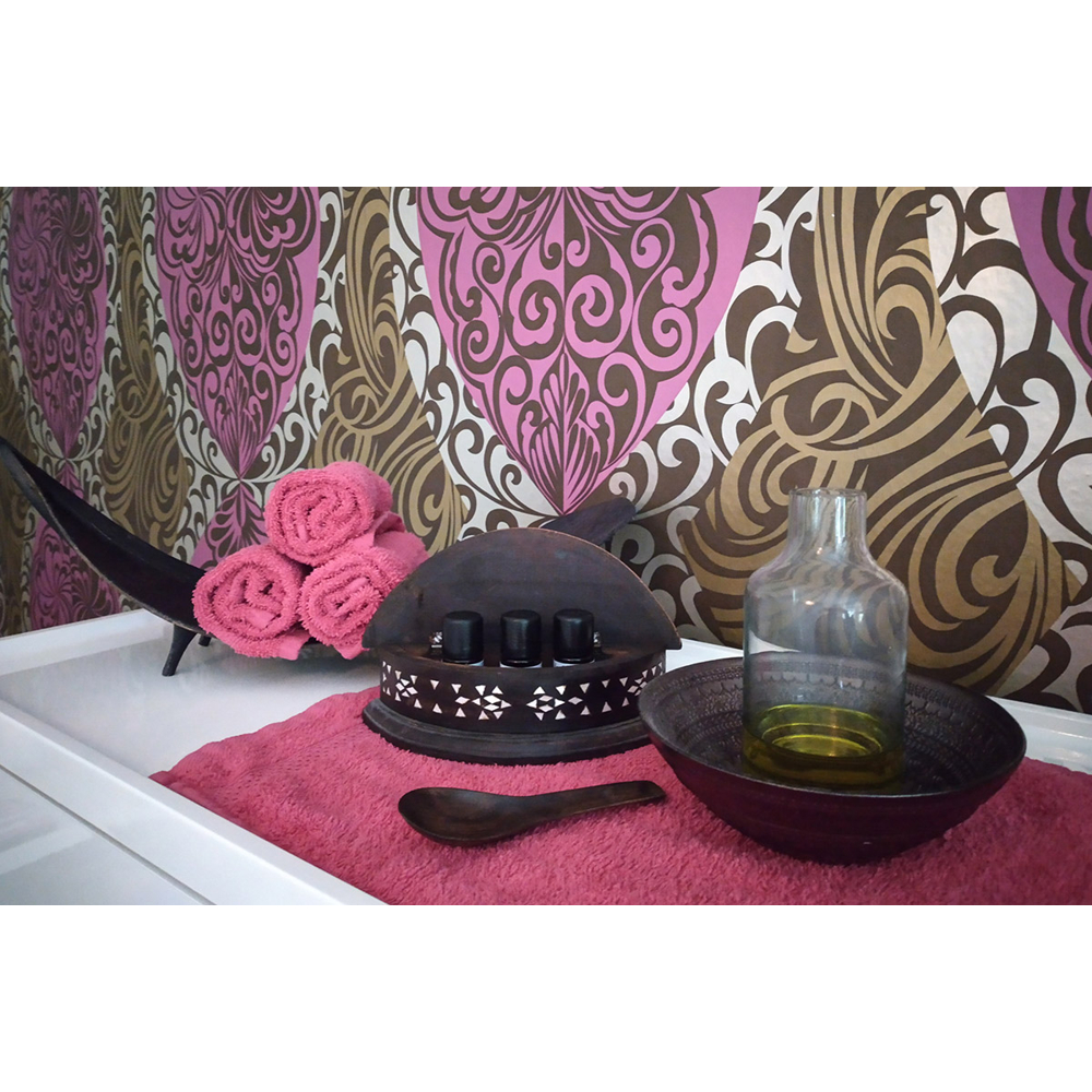 Wellness-Setup mit rosa Handtüchern, Ölfläschchen und Schale vor einer Mustertapete.