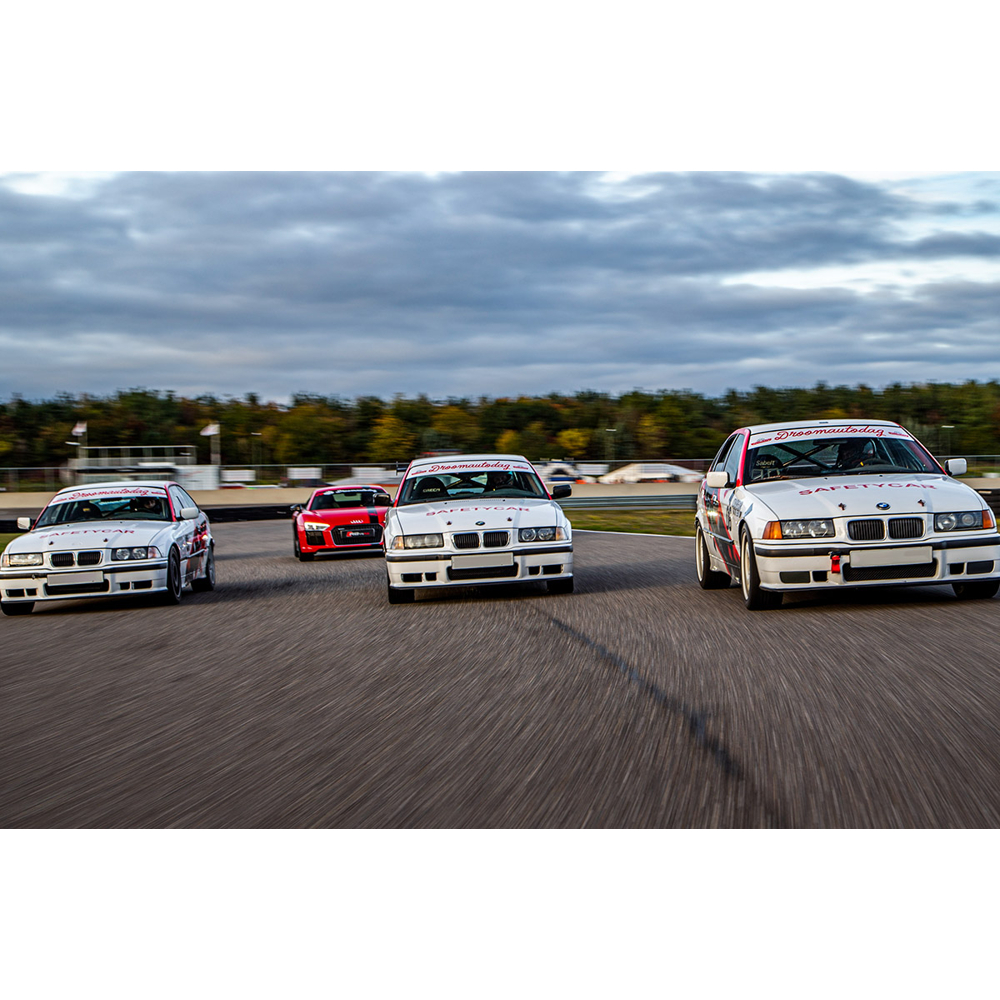 Vier Rennwagen fahren auf einer Strecke, angeführt von drei weißen BMW Safety Cars und einem roten Auto dahinter.