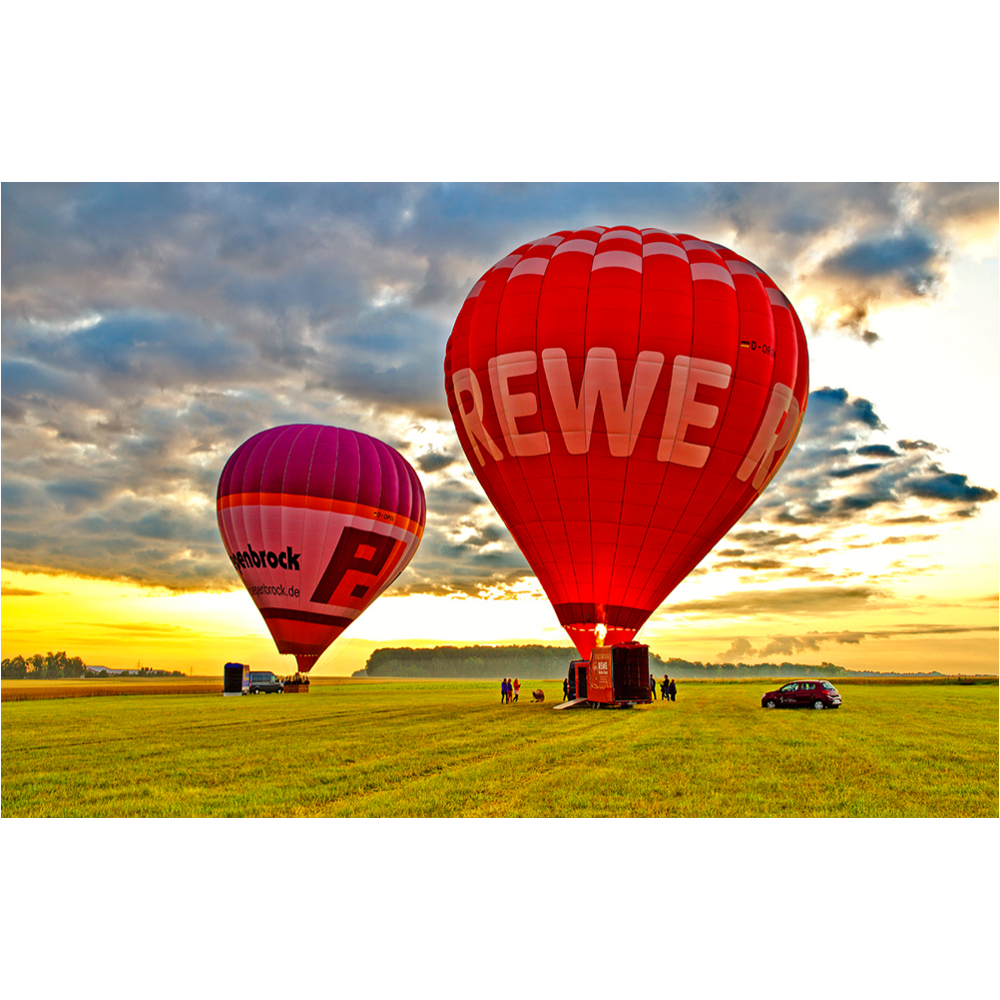 Zwei Heißluftballons in einer grünen Wiesenlandschaft bei Sonnenuntergang.