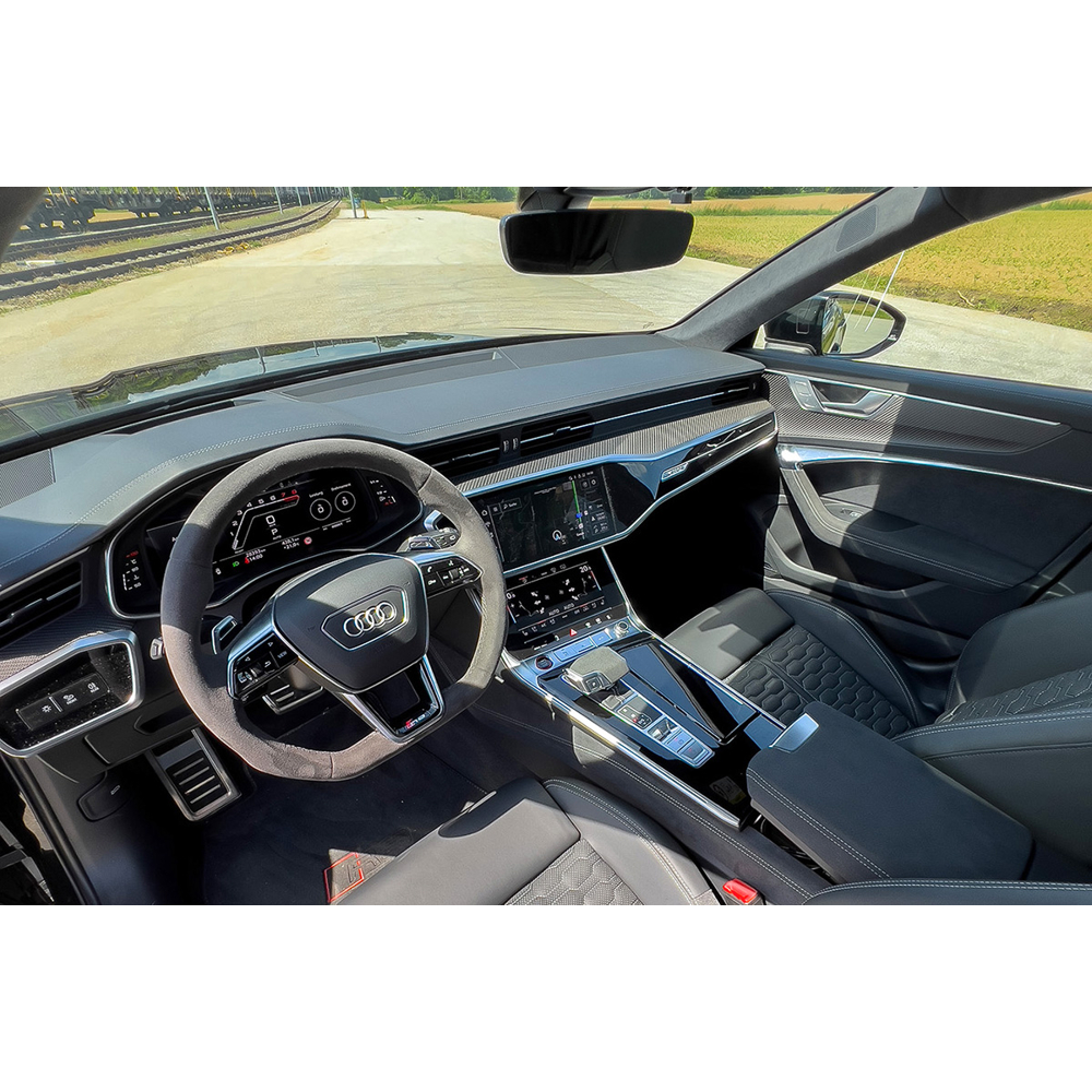 Blick in das moderne, schwarze Interieur eines Autos mit Lenkrad, Displays und Ledersitzen, draußen ist ein Feld.