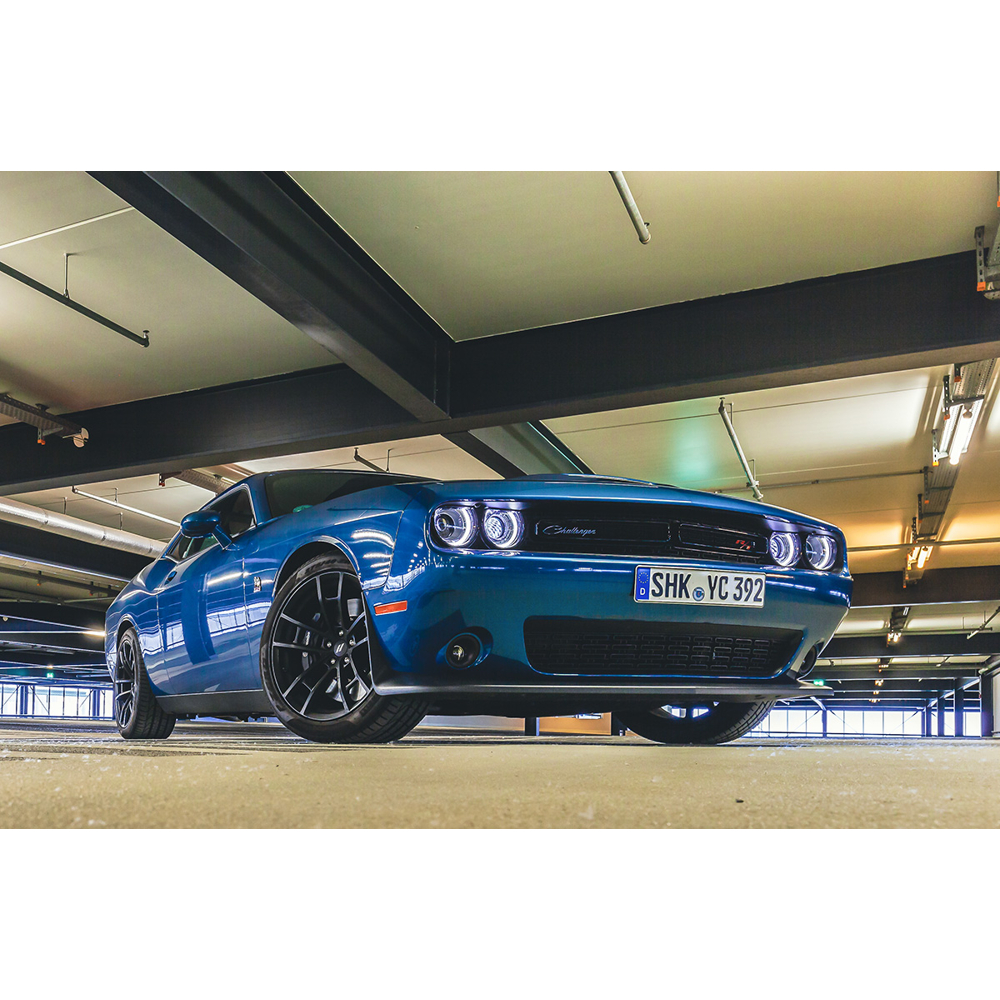 Ein blauer Dodge Challenger steht in einer hellen Tiefgarage unter Betondecken.