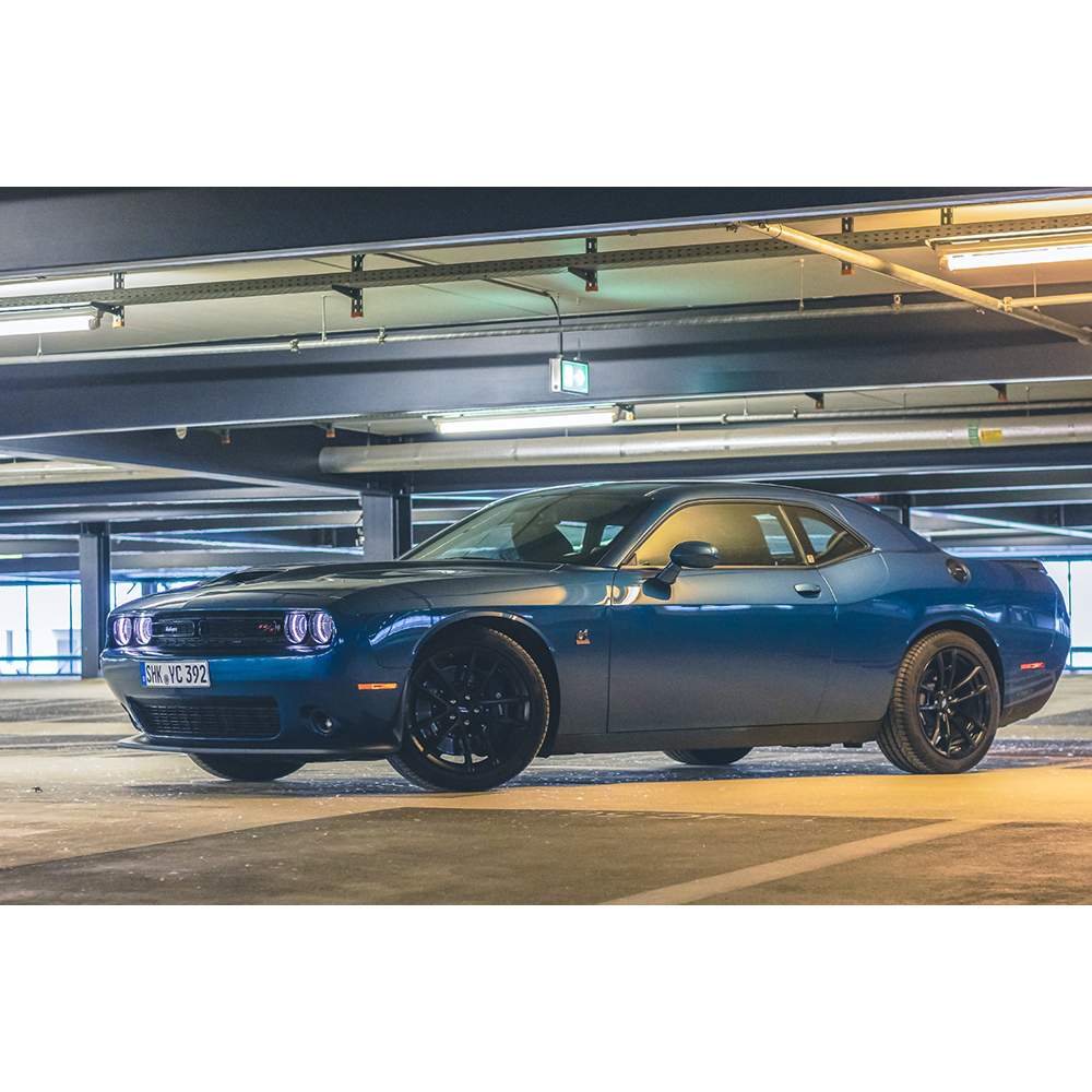 Ein blauer Dodge Challenger parkt in einem hellen, modernen Parkhaus unter Neonröhren.