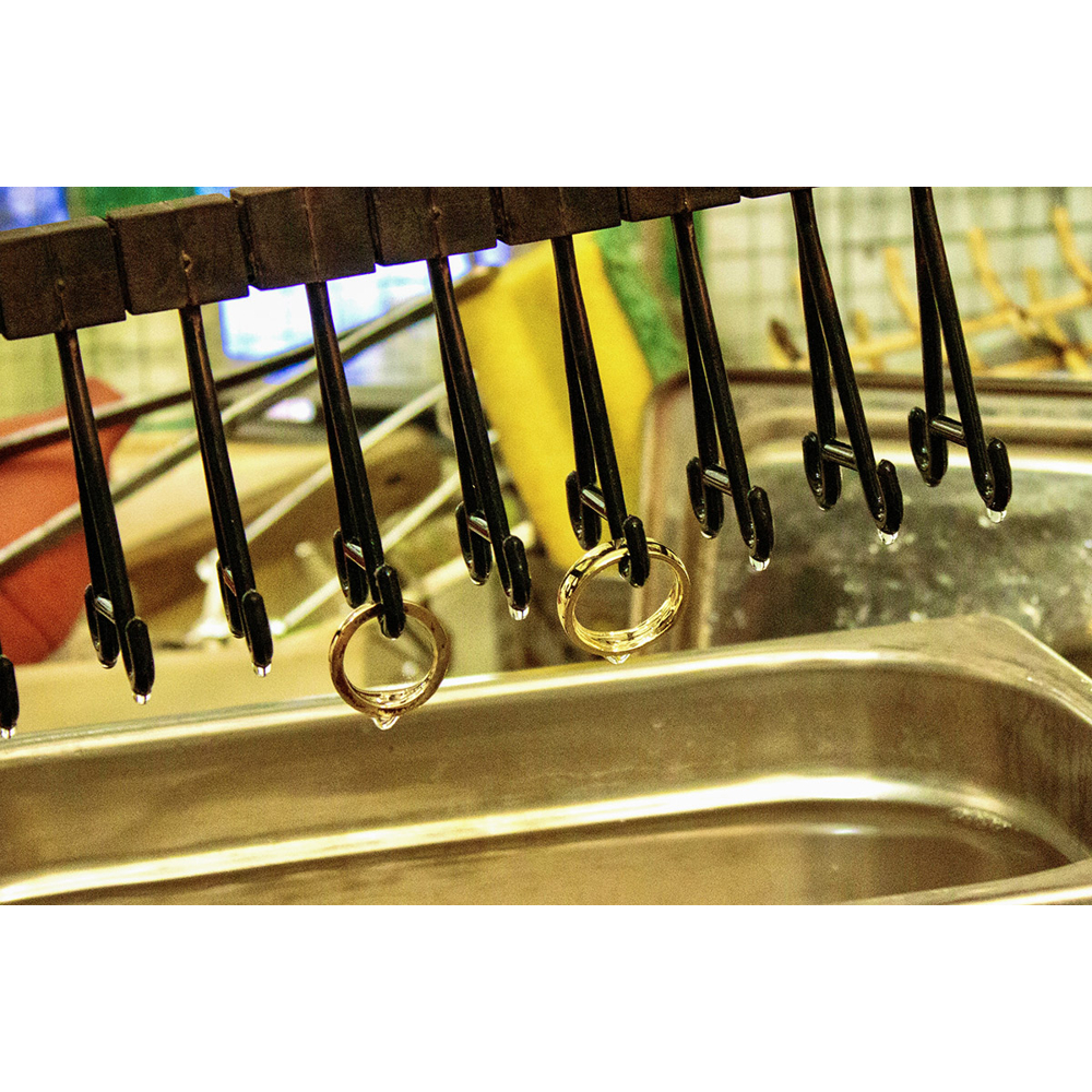 Goldringe hängen in einer Werkstatt an Metallklammern über einem Becken.