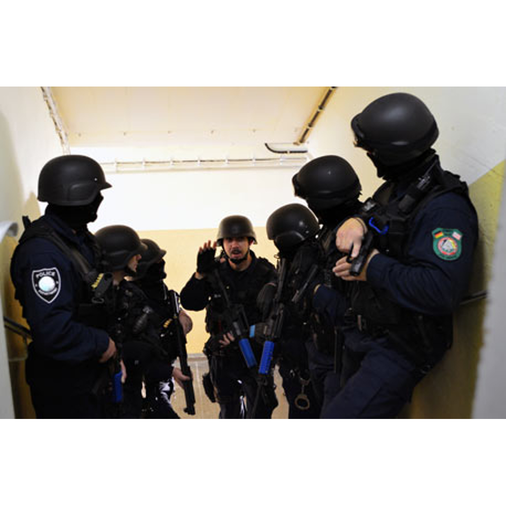 Einsatzkräfte in dunkler Uniform und Helmen halten taktische Waffen in einem Flur.