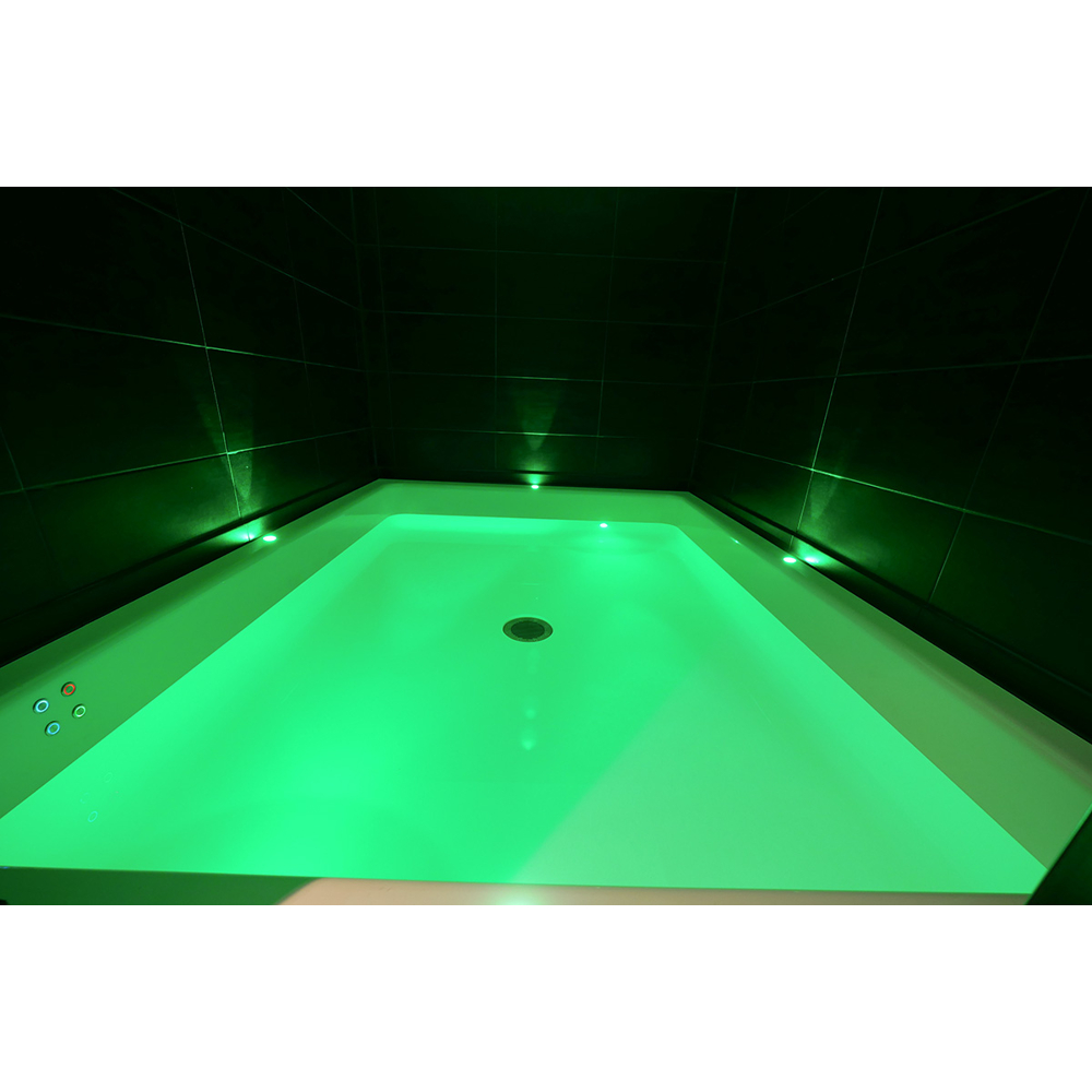 Eine weiße Badewanne mit leuchtend grünem Wasser, vor dunklen Fliesenwänden in einem gedimmten Raum.