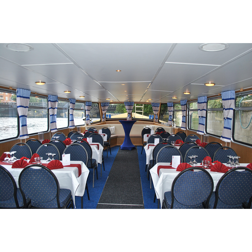 Elegantes Schiffsrestaurant mit blau-weißen Sesseln, eingedeckten Tischen, roten Servietten und großen Fenstern mit Flussblick.