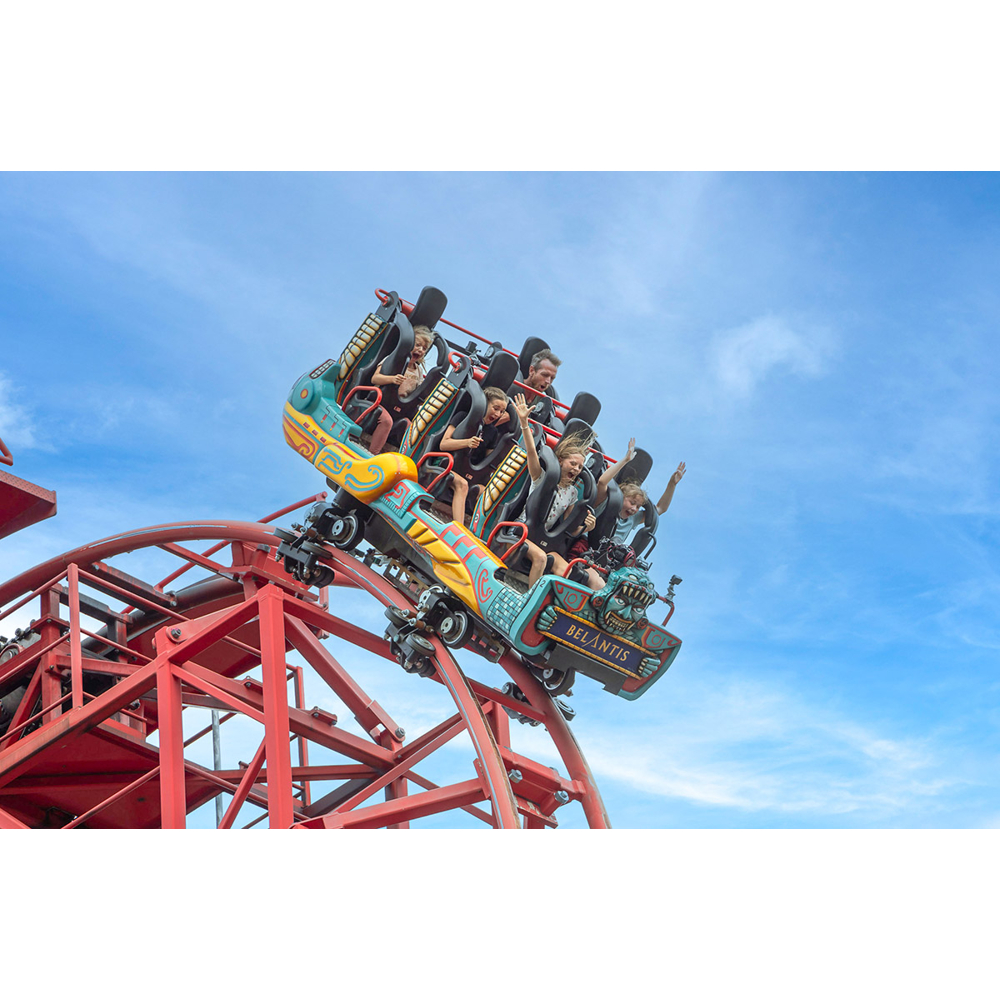 Menschen fahren auf einer bunten Achterbahn mit roter Schiene vor blauem Himmel.