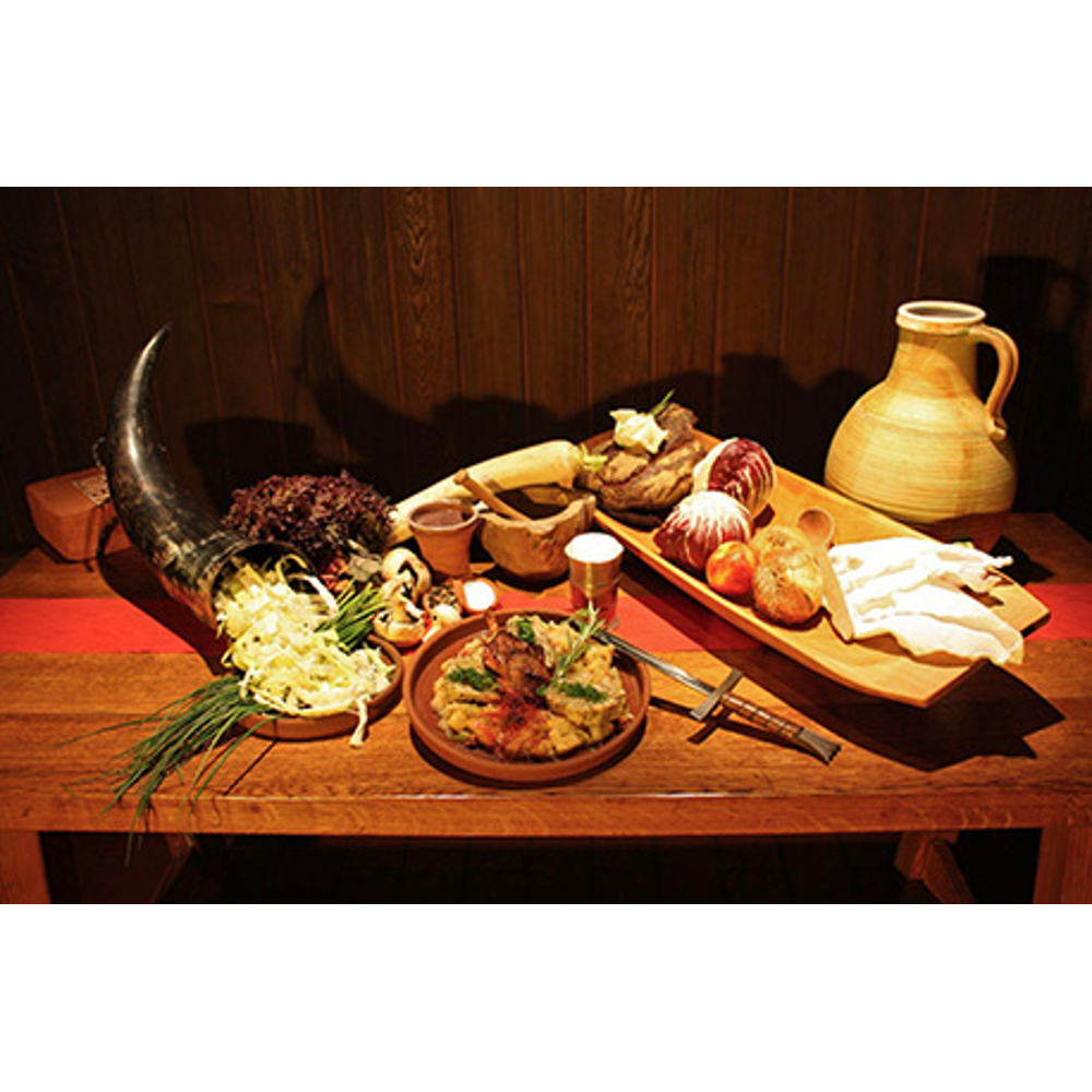 Rustikales Bankett auf Holzisch mit Fleisch, Gemüse, Krug und Horn vor Holzwand.