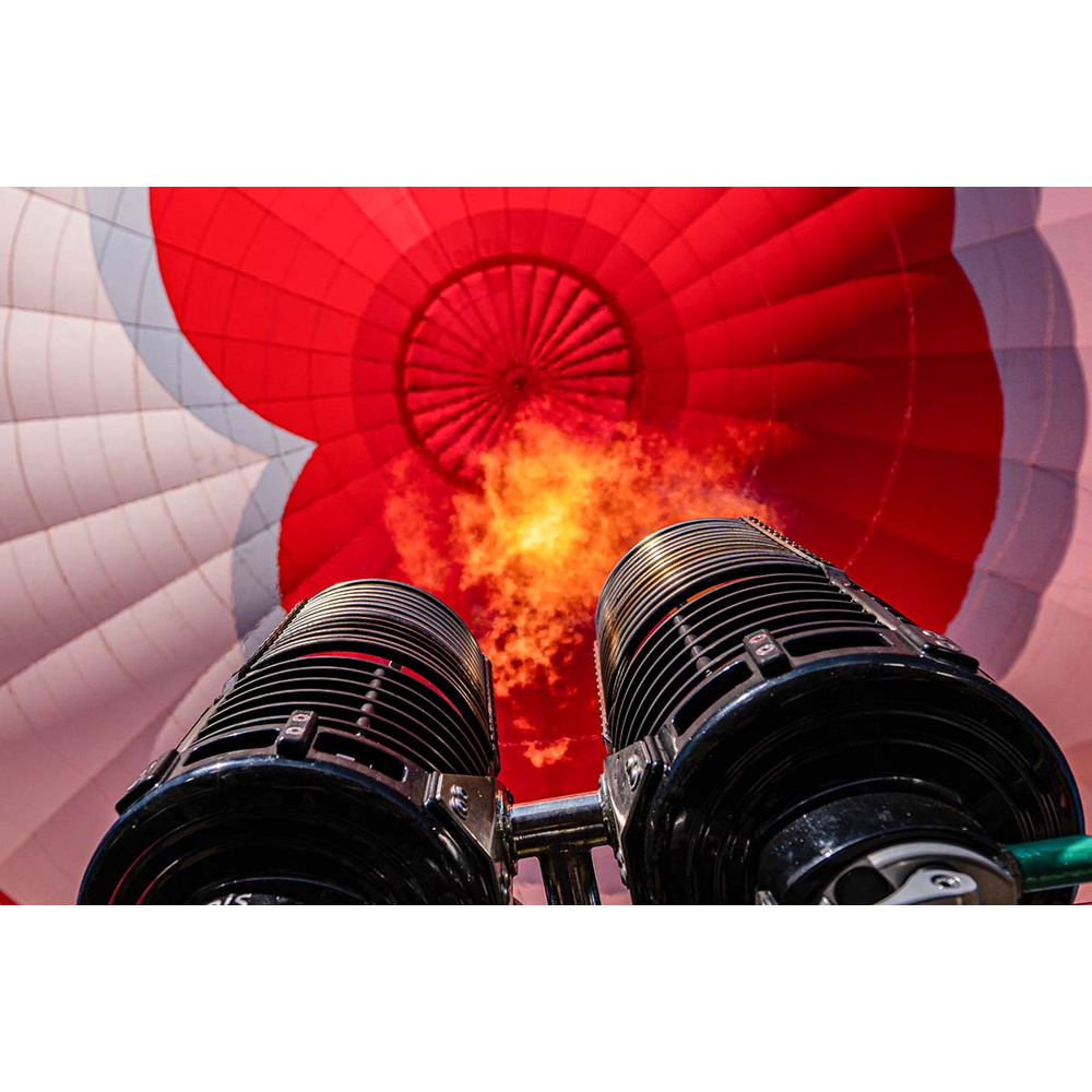 Blick nach oben auf einen Heißluftballonbrenner mit Flamme und rot-weißem Ballonstoff.