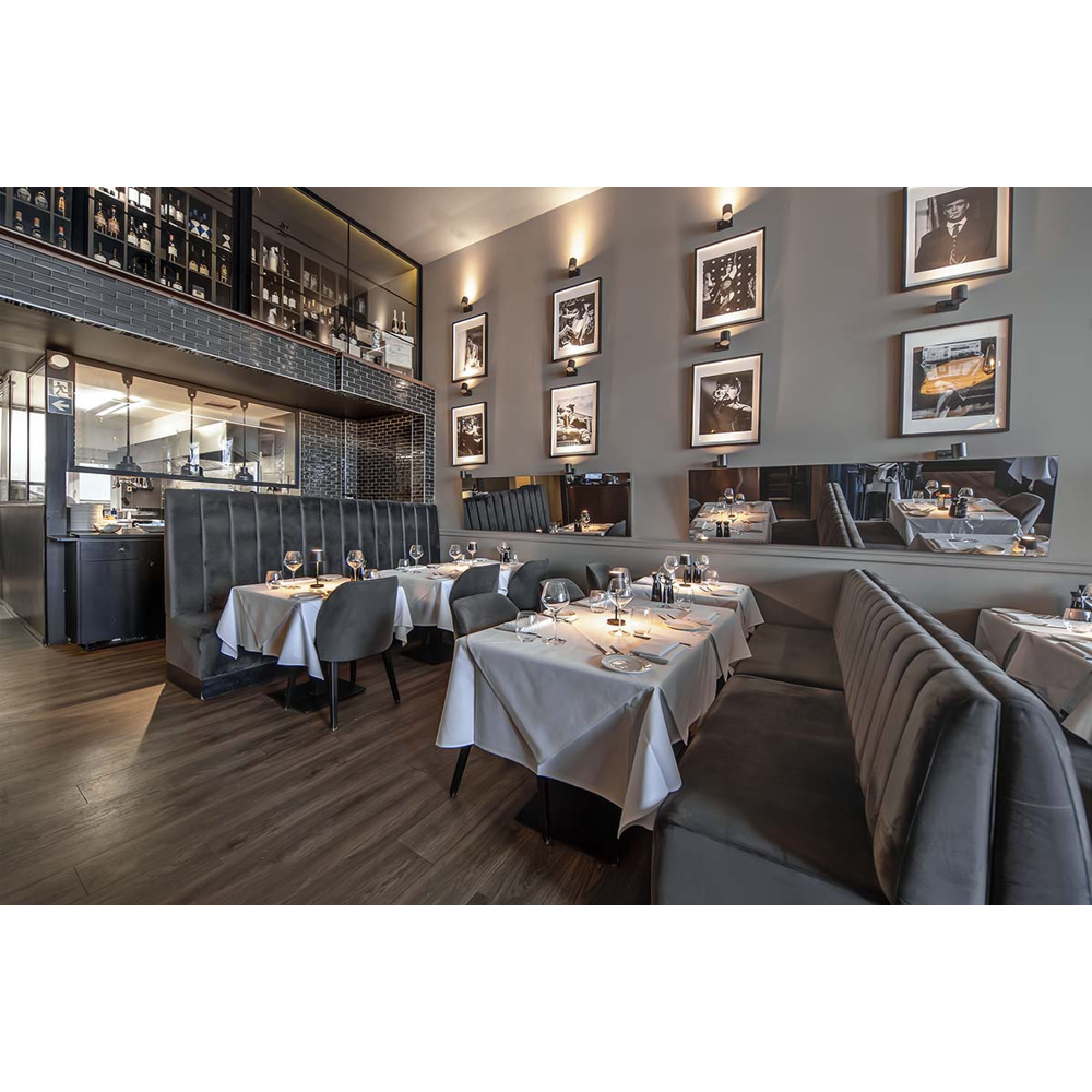 Ein modernes Restaurant mit grauen Wänden, gepolsterten Bänken, gedeckten Tischen und gerahmten Fotos.