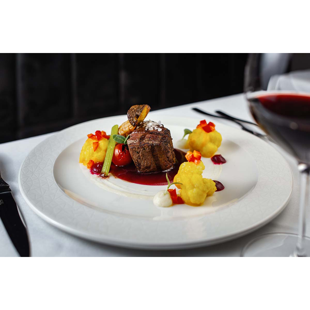 Filetsteak mit Beilagen und Rotweinsoße auf einem weißen Teller, daneben ein Glas Rotwein.