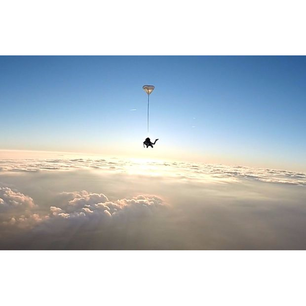 Ein Fallschirmspringer fällt am hellen Himmel über einer dichten Wolkendecke.
