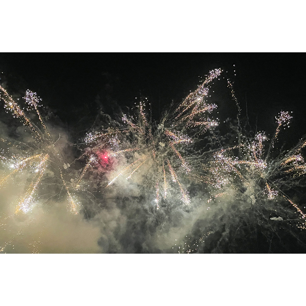 Brillante weiße und goldene Feuerwerkskörper explodieren am dunklen Nachthimmel und erzeugen helle Spuren.