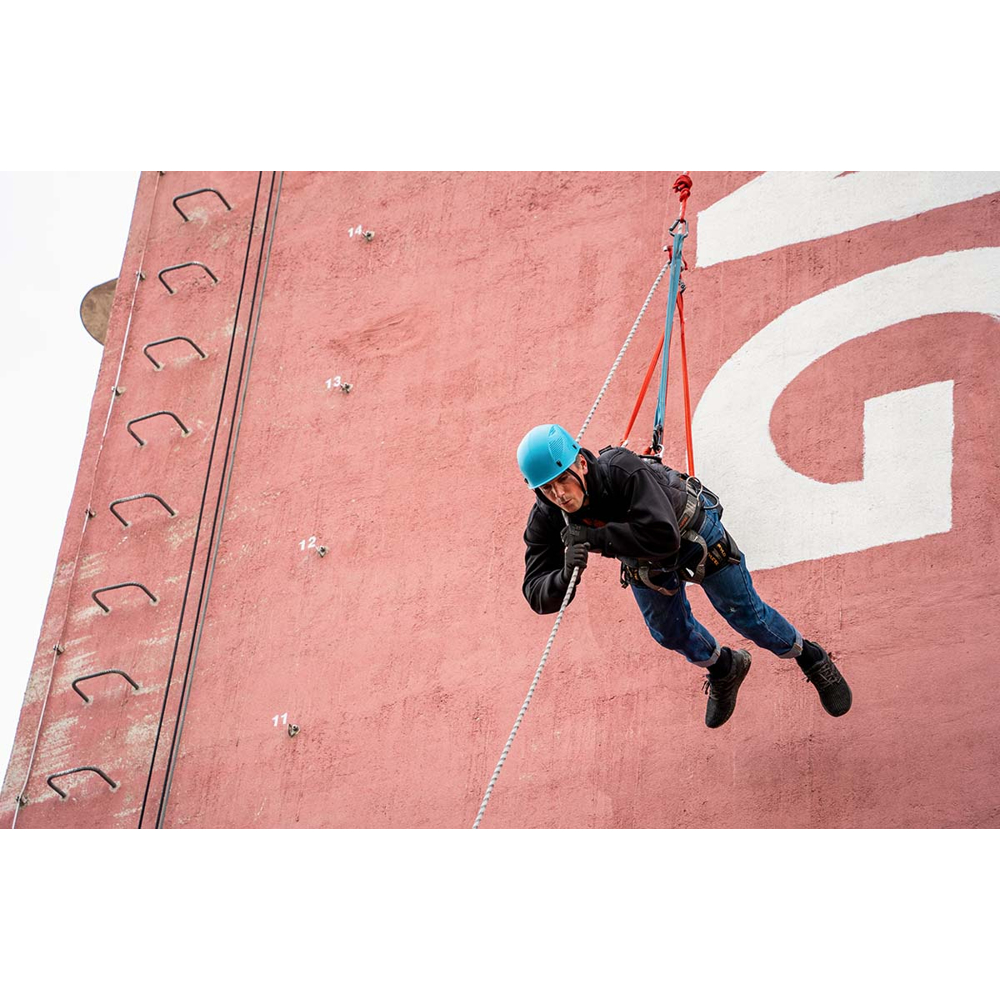 Ein Kletterer mit blauem Helm und Seilen an einer roten Wand.