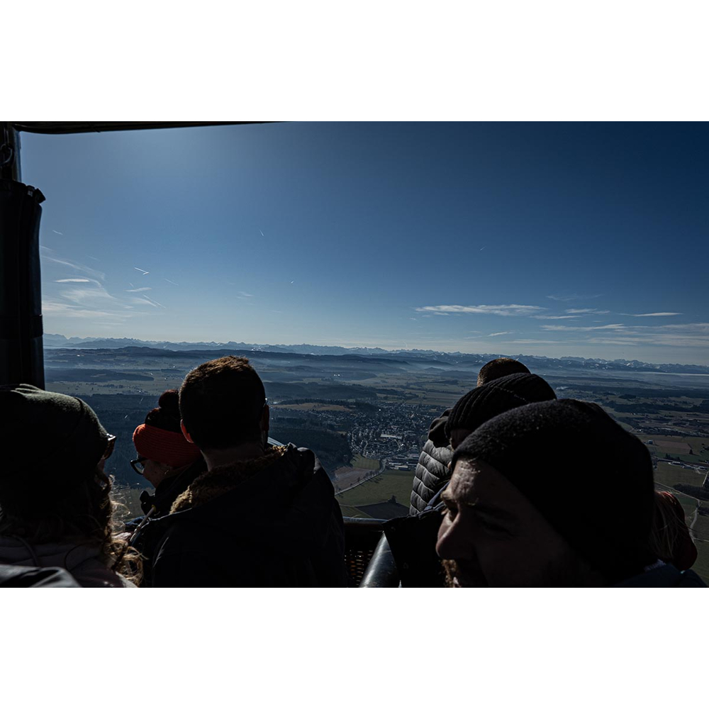 Menschen im Heißluftballonkorb blicken unter klarem blauem Himmel auf entfernte Berge.