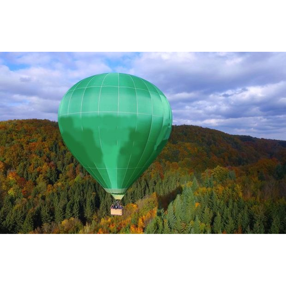 Ein grüner Heißluftballon fliegt über einen herbstlichen Wald unter einem wolkigen Himmel.