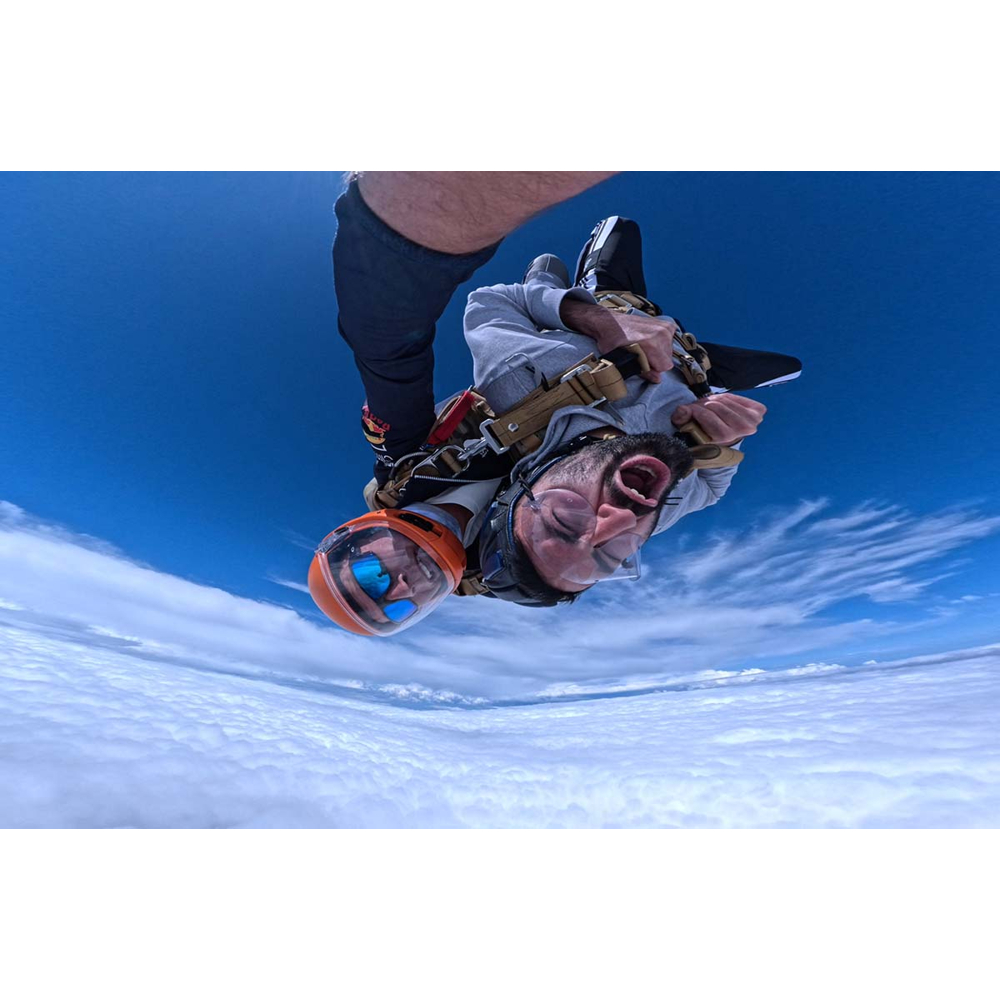 Zwei Fallschirmspringer fallen durch die Luft, mit blauem Himmel im Hintergrund und weißen Wolken unter ihnen.
