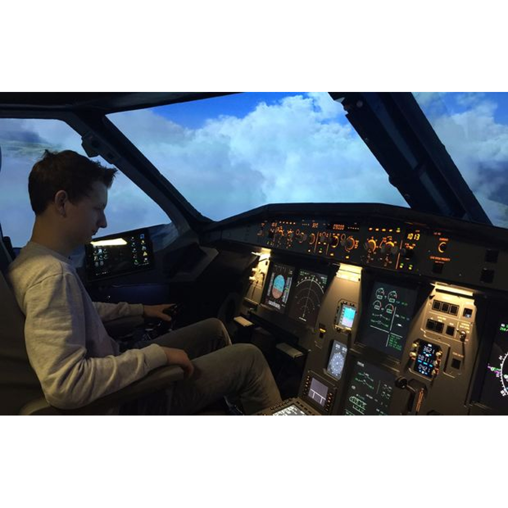 Ein junger Mann sitzt im Cockpit eines Flugsimulators und blickt auf Steuerelemente, draußen ist ein bewölkter Himmel.