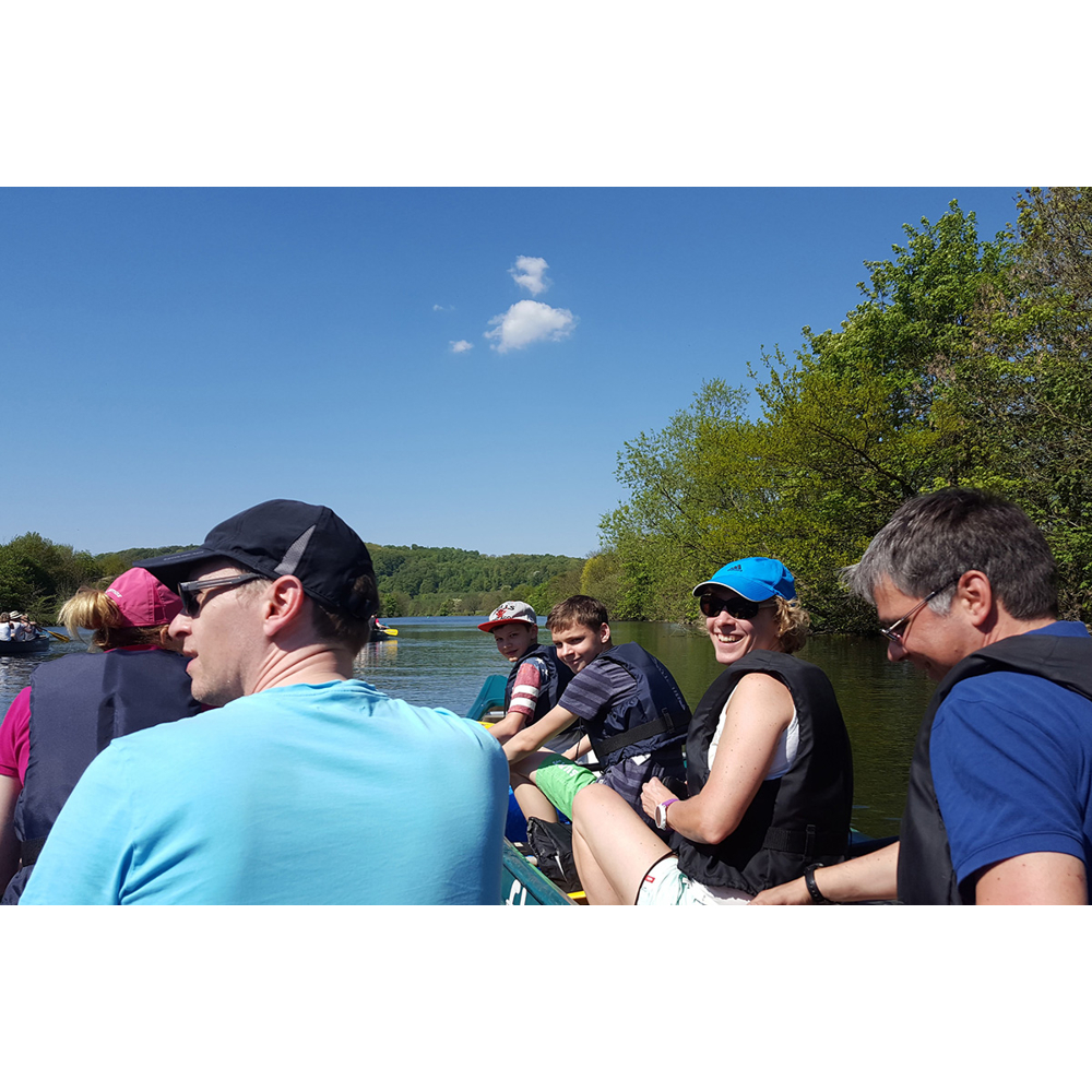 Eine Gruppe von Menschen genießt an einem sonnigen Tag eine Bootsfahrt auf einem ruhigen Fluss.