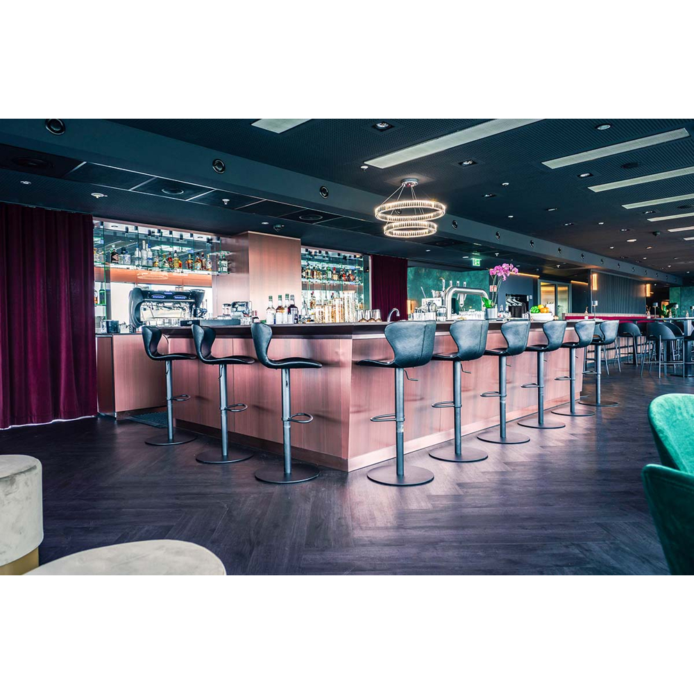 Moderne Bar mit beleuchteter Theke, schwarzen Barhockern, Holzboden und dunkler Decke.