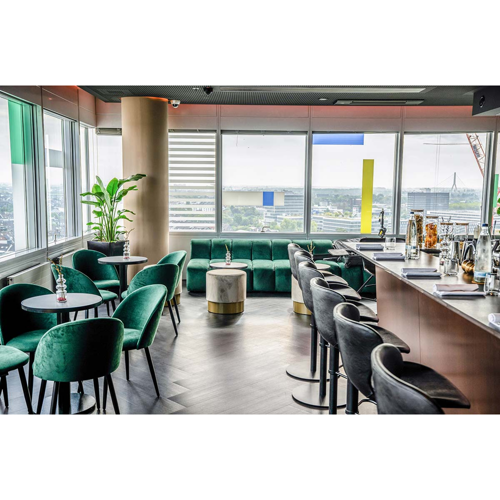Moderne Bar mit grünen Samtsesseln, Tischen, einer langen Theke und grossen Fenstern mit Ausblick.