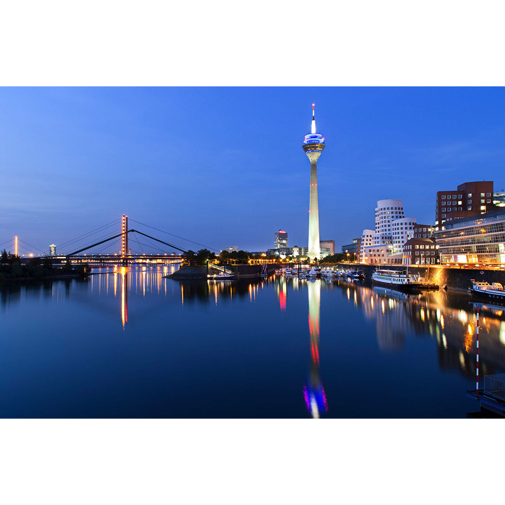 Abendlicher Blick auf den Rheinturm und die beleuchtete Brücke in Düsseldorf mit Flussspiegelung.