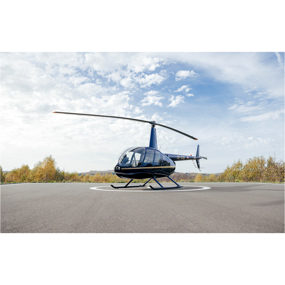 Ein blauer Hubschrauber steht auf einem grauen Landeplatz unter einem bewölkten Himmel.