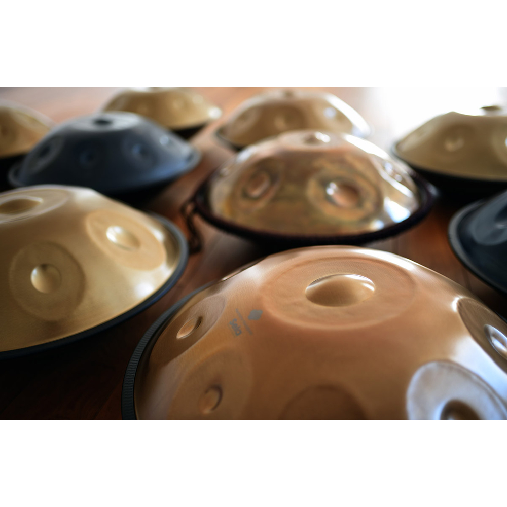Eine Sammlung von Handpans aus Bronze und Schwarz auf einer Holzoberfläche.