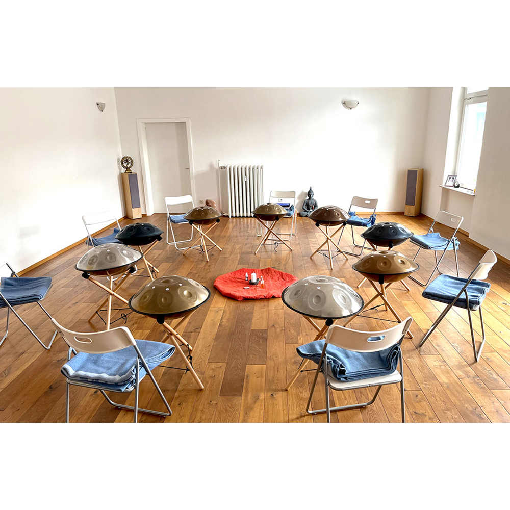 Handpans auf Ständern in einem Kreis mit Stühlen und einer roten Matte in einem hellen Raum.