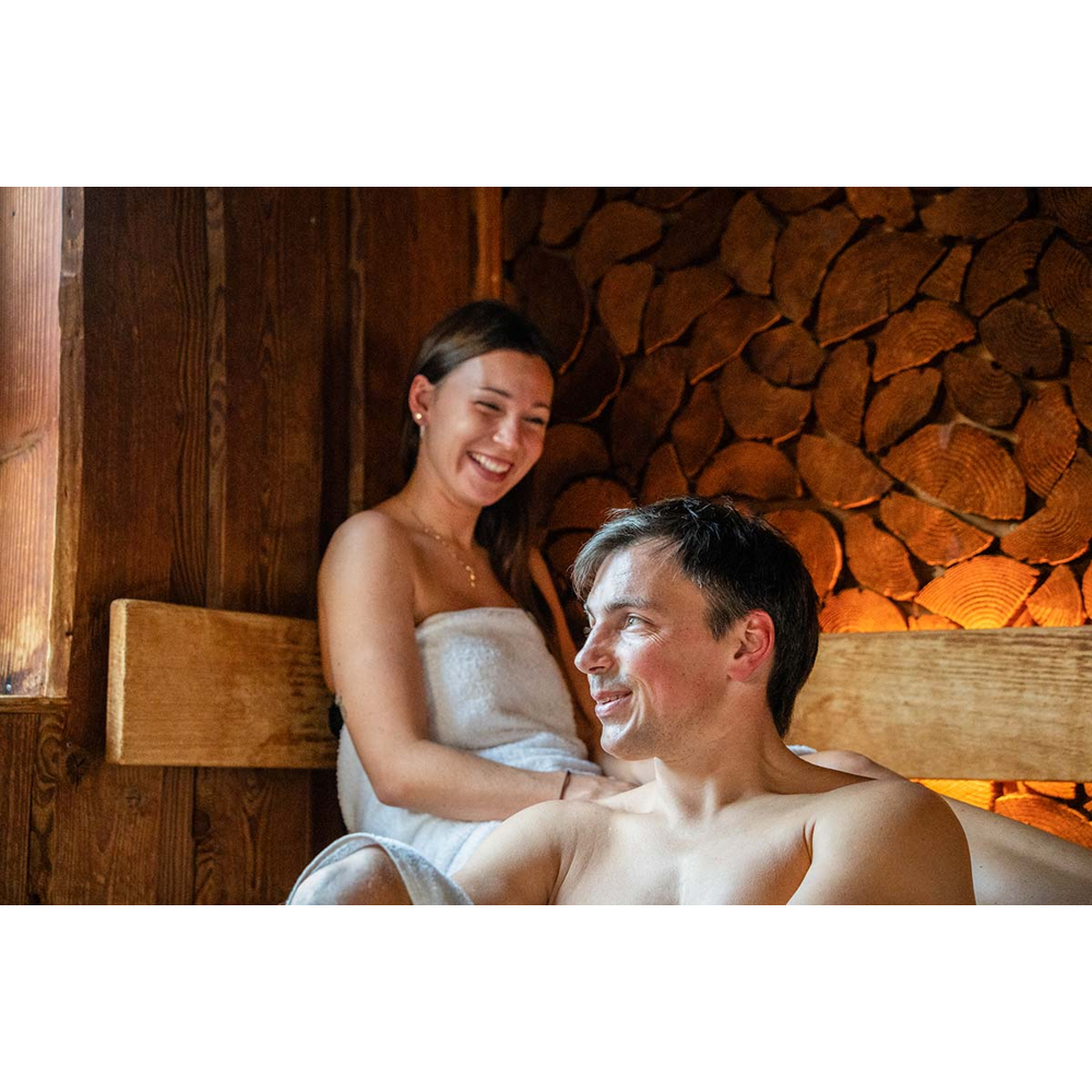 Ein Mann und eine lächelnde Frau in Handtüchern entspannen auf Holzbänken in einer Sauna.