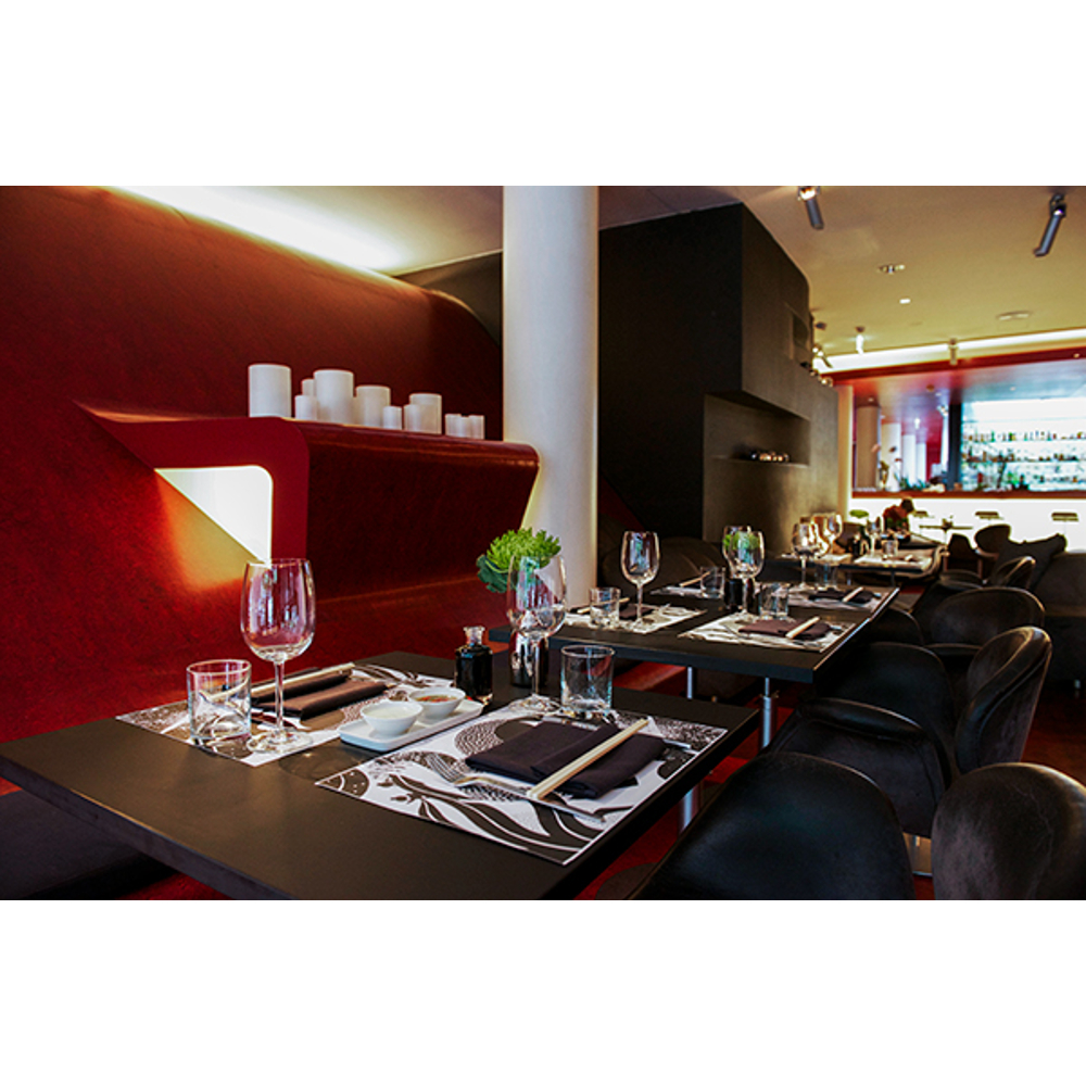 Ein modernes Restaurant mit dunklen Tischen, schwarzen Stühlen, Weingläsern und einer roten Wand mit Kerzen.