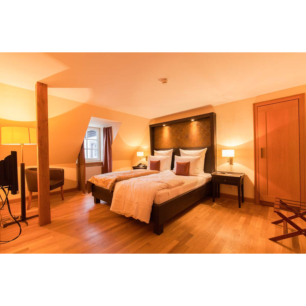 Gemütliches Hotelzimmer mit großem Doppelbett, Holzböden, Nachttischen, Stehlampe, Sesseln und Fenster.