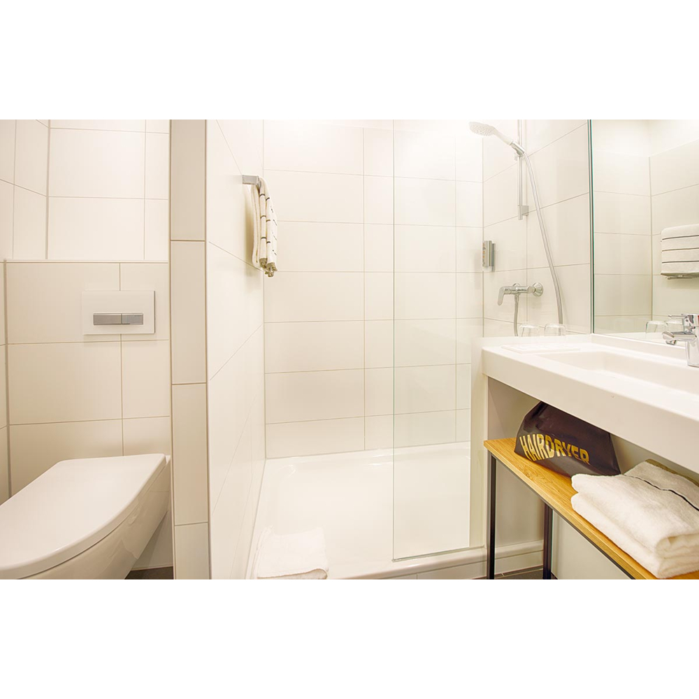 Modernes weißes Badezimmer mit Dusche, Toilette, Waschbecken und ordentlich gefalteten Handtüchern.