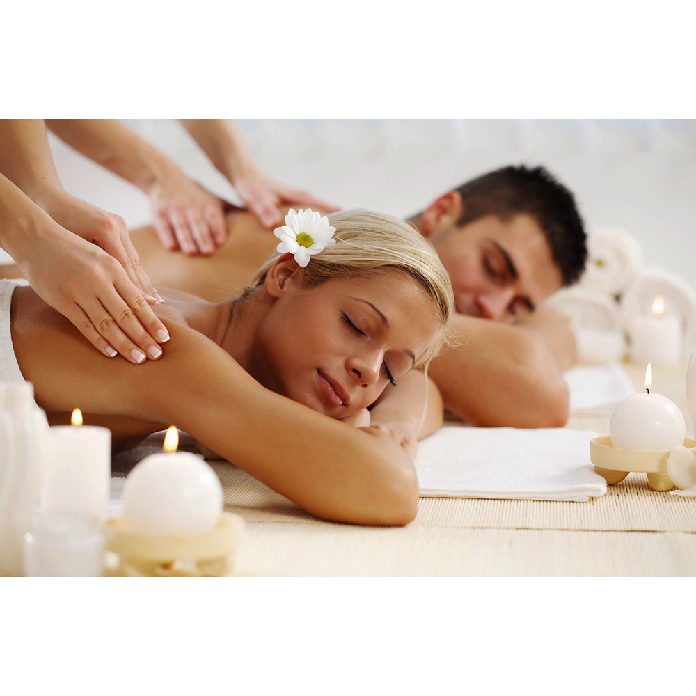 Eine Frau mit einer Blume im Haar genießt eine entspannende Partnermassage bei Kerzenschein.