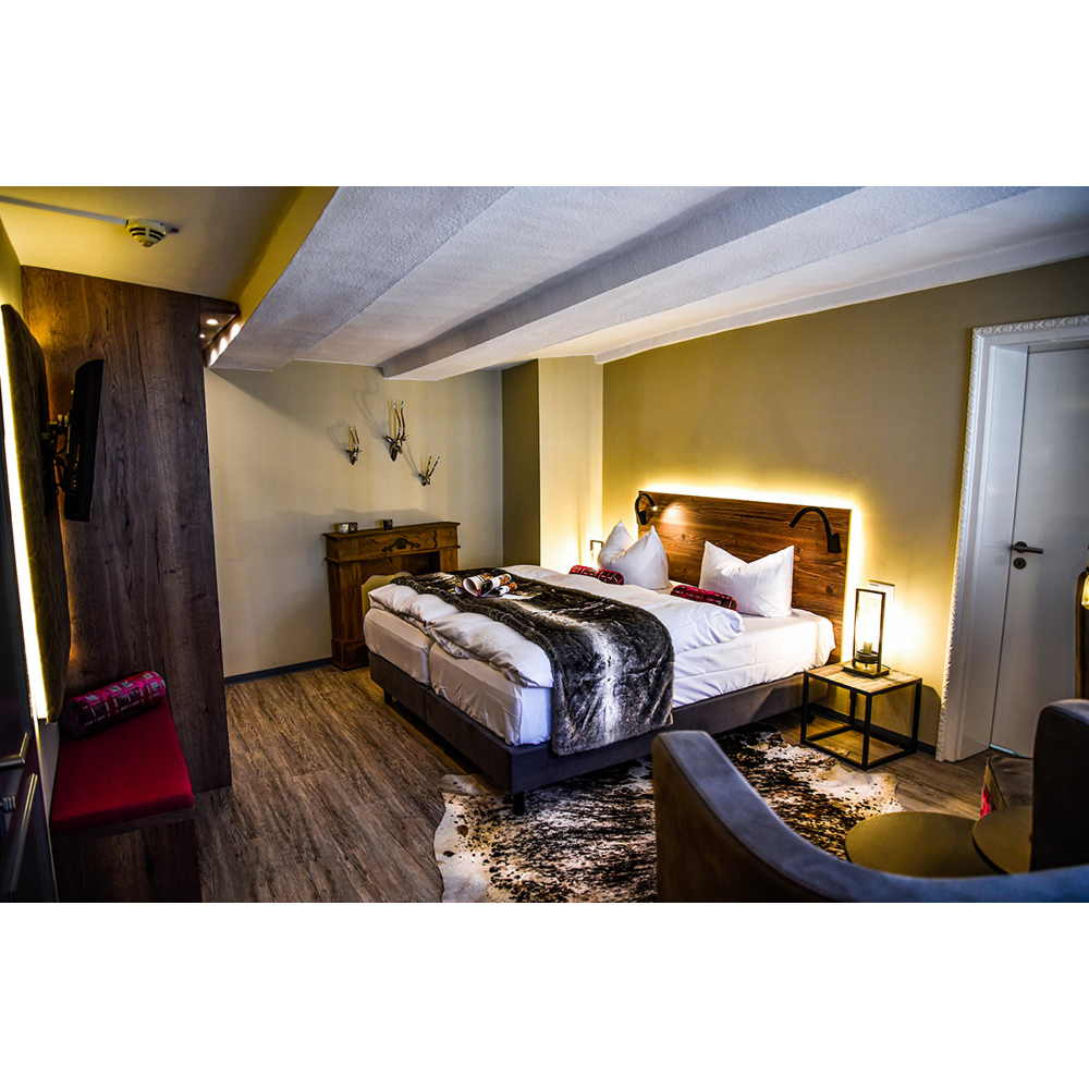 Gemütliches Hotelzimmer mit großem Bett, Holzwänden, warmem Licht und Kuhfellteppich.