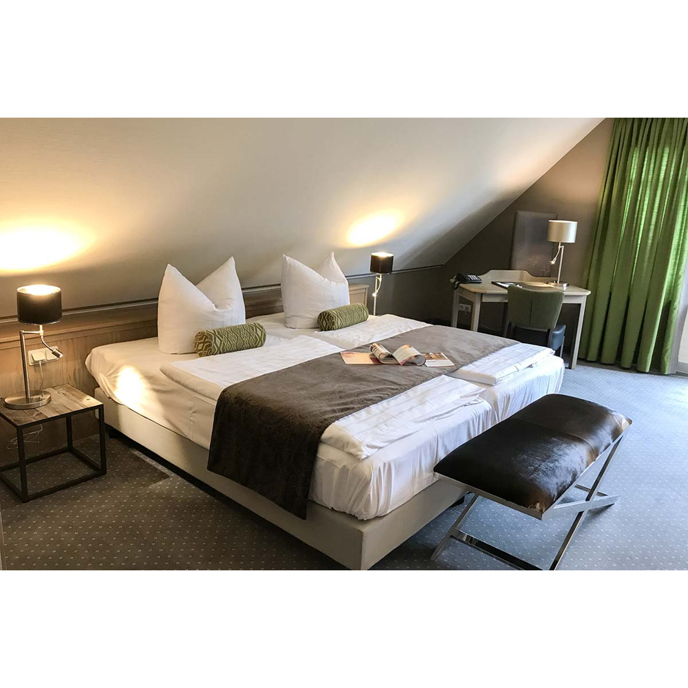 Gemütliches Dachzimmer mit großem Doppelbett, Nachtischen, Leselampe, Schreibtisch und grünen Vorhängen.