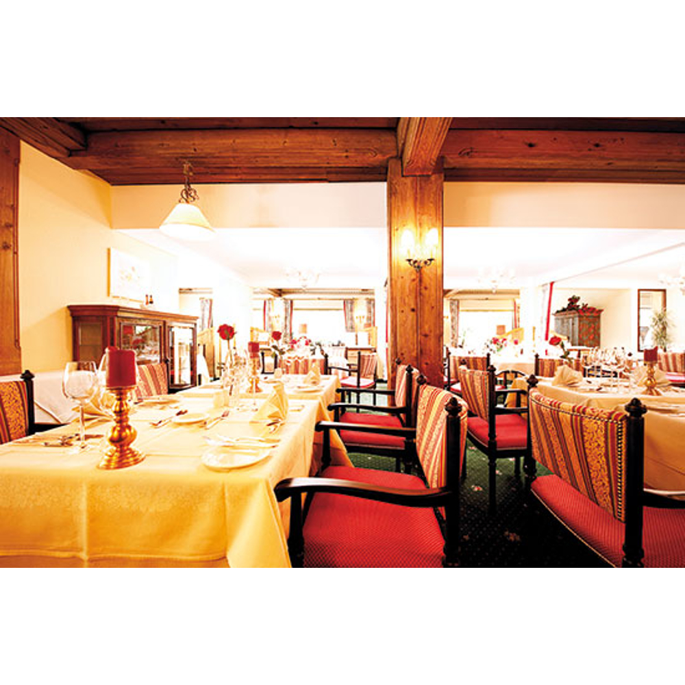 Ein warmes Restaurantinnere mit Holzbalken, weiß gedeckten Tischen und Stühlen mit rot-gold gestreiftem Stoff.