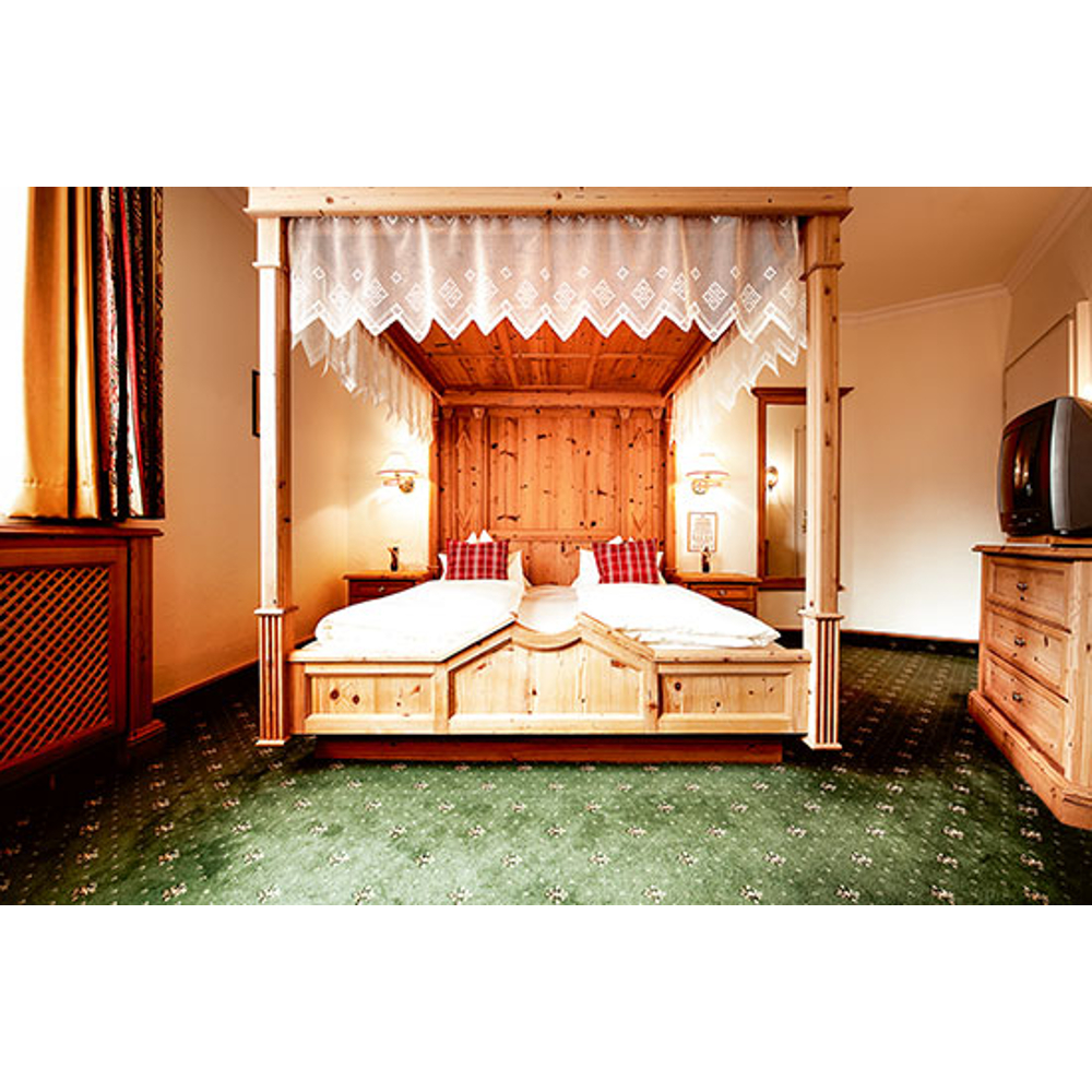 Gemütliches Schlafzimmer mit großem Holzhimmelbett, grünem Teppich und Holzkästchen mit Fernseher.