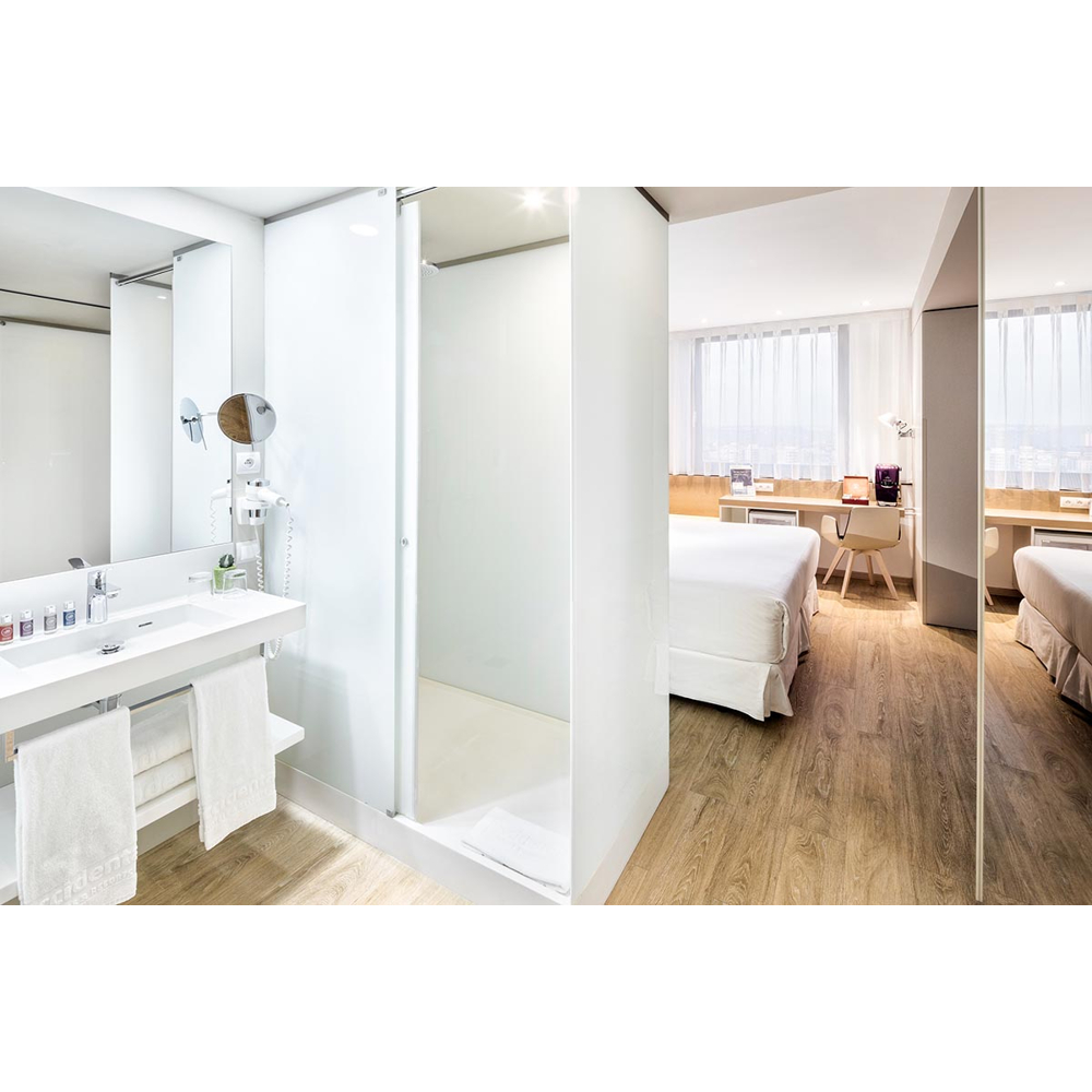 Ein modernes Hotelzimmer mit offenem Bad, Waschbecken, Dusche und Bett im Hintergrund.