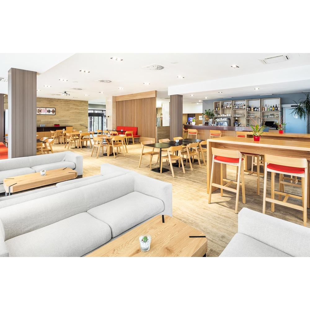 Moderne Hotellobby mit hellen Sofas, Holztischen, Stühlen und einer Bar im Hintergrund.