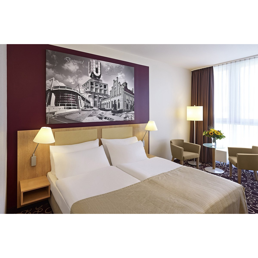 Hotelzimmer mit einem großen Doppelbett, zwei Nachttischlampen, einem Schwarz-Weiß-Wandbild und zwei Sesseln.