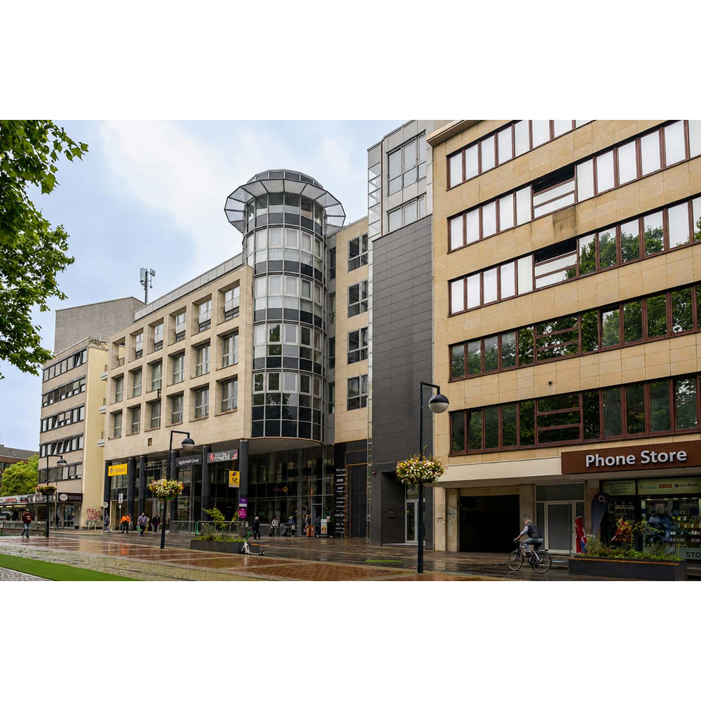 Eine moderne Stadtstraße mit hohen Buerogebäuden, einem zylindrischen Glassturm, Fußgaengern und einem Fahrradfahrer.