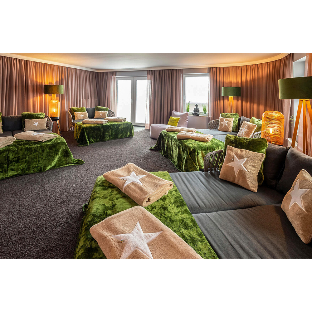 Ein Ruheraum mit grauen Sofas, grünen Samtdecken und Kissen mit weißen Sternen bei warmer Beleuchtung.