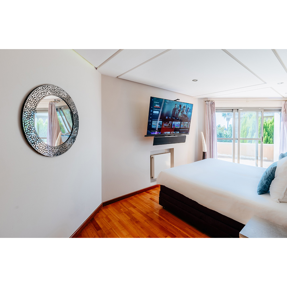 Moderne Schlafzimmereinrichtung mit grossem Spiegel, Flachbildfernseher an der Wand und hellem Holzboden.