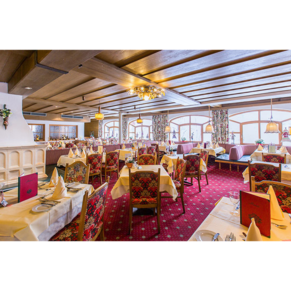 Rustikales Restaurant mit Holzdecken, rotem Teppich und gedeckten Tischen mit weißen Tüchern und Speisekarten.