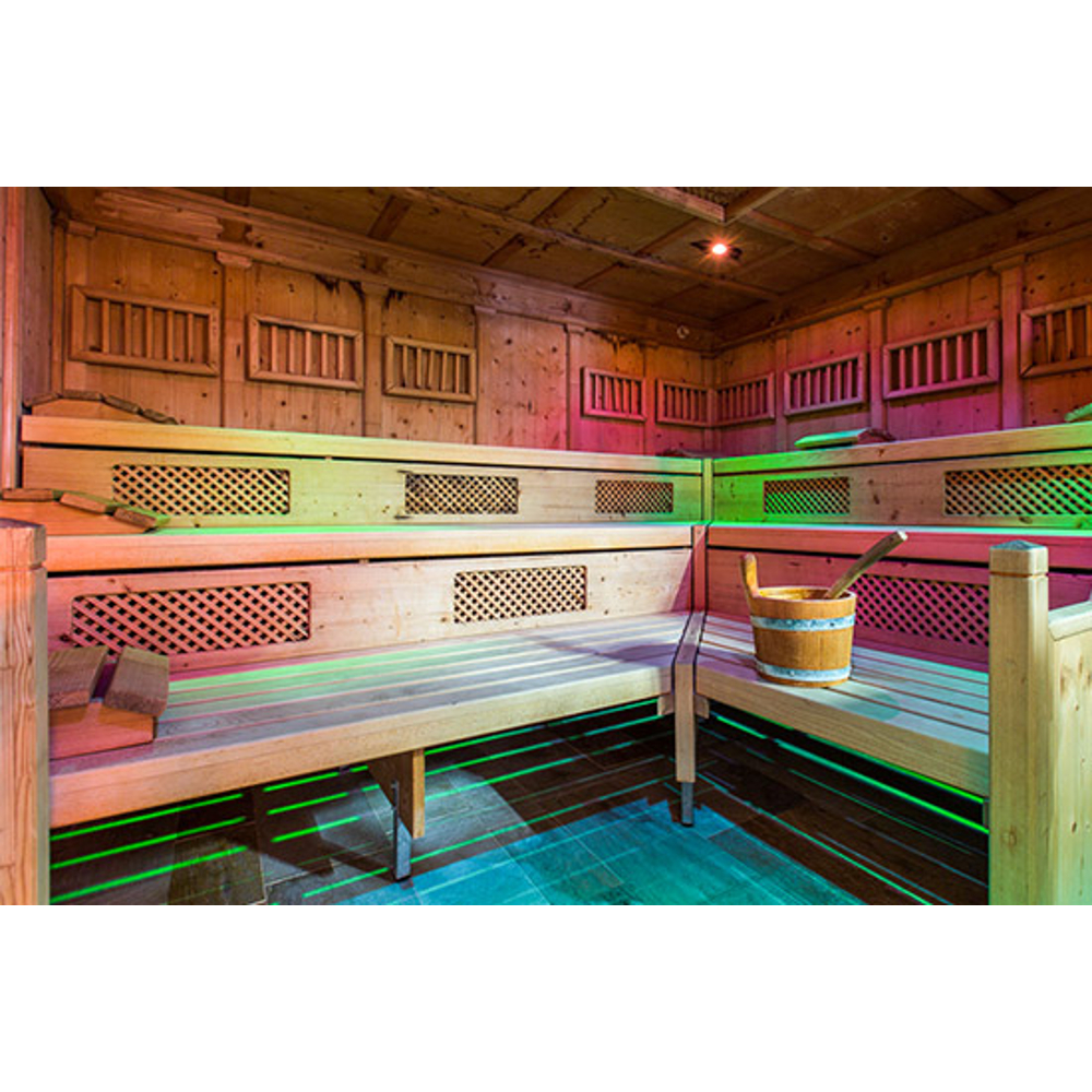 Holzsauna mit gestuften Bänken, grünem Licht unten und einem Eimer mit Kelle.