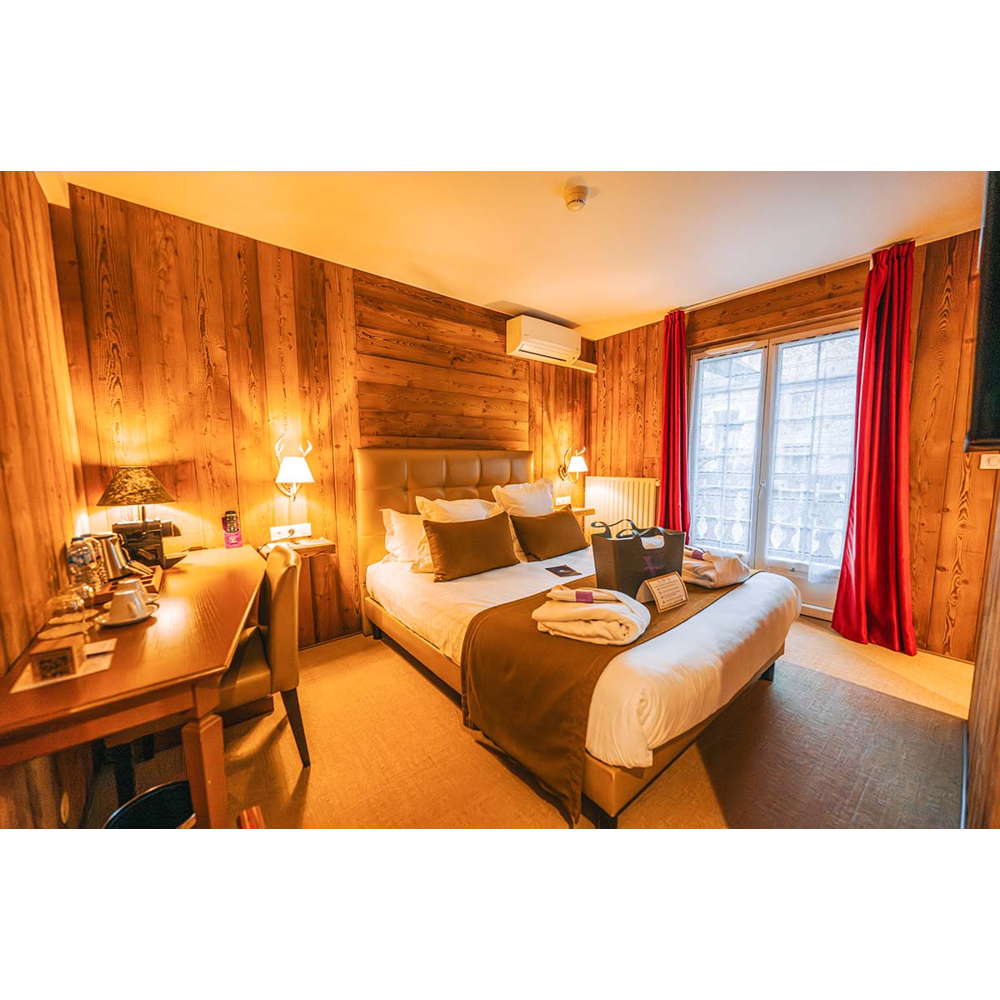 Gemütliches Schlafzimmer mit holzverkleideten Wänden, großem Bett, Schreibtisch und roten Vorhängen an der Balkontür.