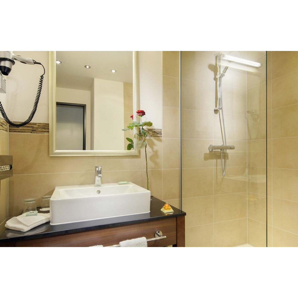 Modernes Badezimmer mit weißem Waschbecken, beleuchtetem Spiegel, roter Rose und einer Glasdusche mit beigen Fliesen.