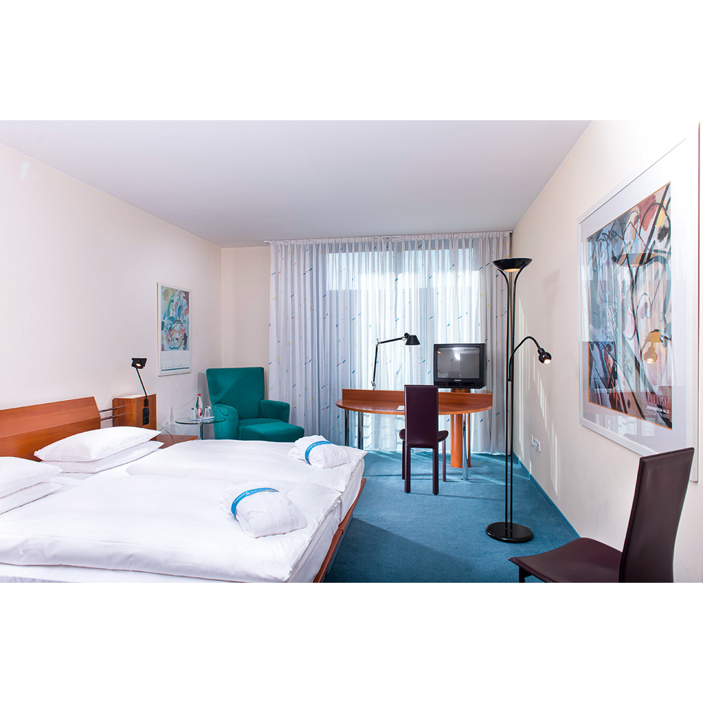 Ein modernes Hotelzimmer mit einem großen Bett, Schreibtisch, Fernseher, Stühlen und blauen Teppichböden.
