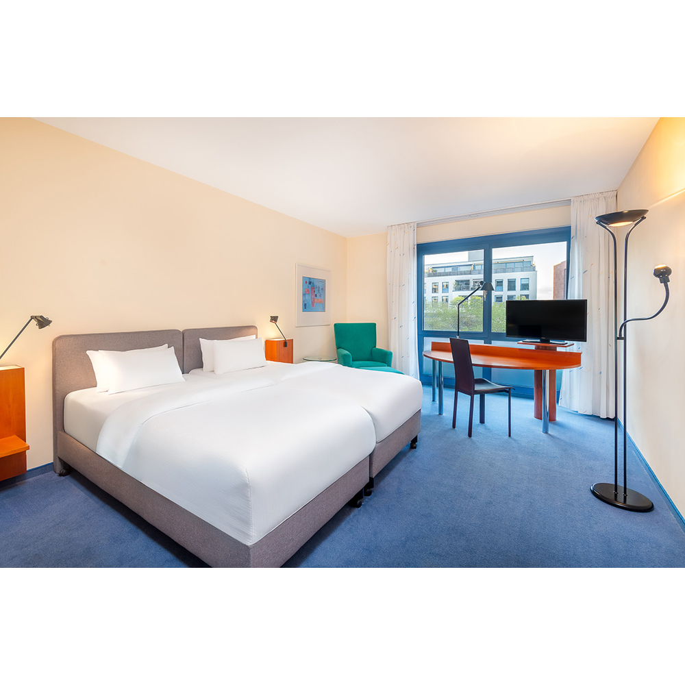 Ein modernes Hotelzimmer mit großem Doppelbett, Schreibtisch mit Fernseher und blauer Teppichboden.